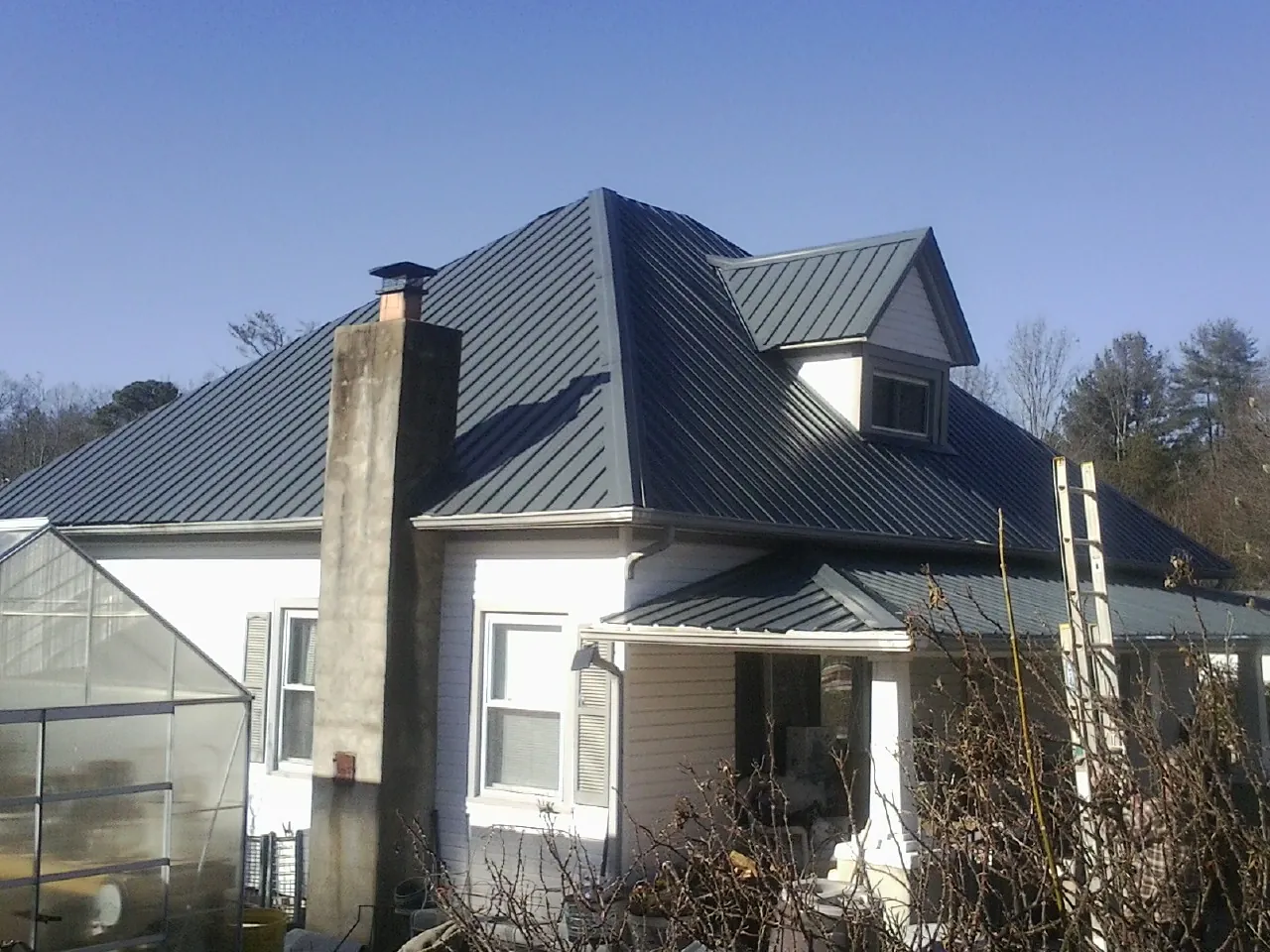 Dark blue standing seam metal roof on a white farmhouse with dormer — Slate & Tile Roof Repair by Roofing Brothers in Reinholds