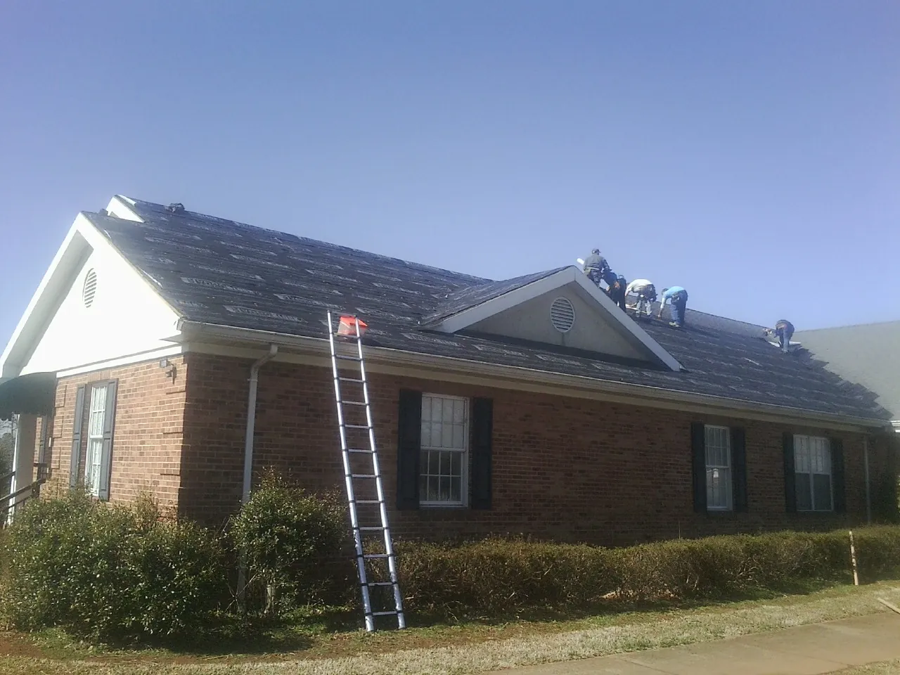 Crew tearing shingles off a brick ranch roof with a ladder set — Metal Roof Repair work by our crew in Reinholds