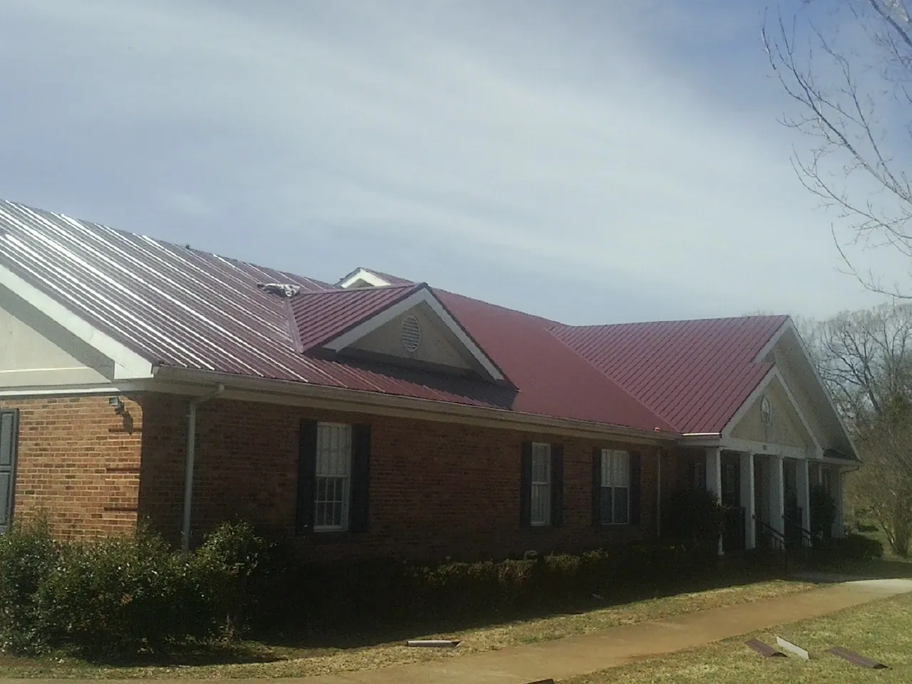 Red metal roof with gabled entries on a long brick building, from a Hail Damage Roof Repair job in Reinholds