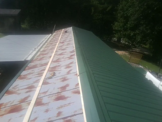Old rusted panels beside newly installed green metal roofing — Wind Damage Roof Repair by Roofing Brothers in Reinholds