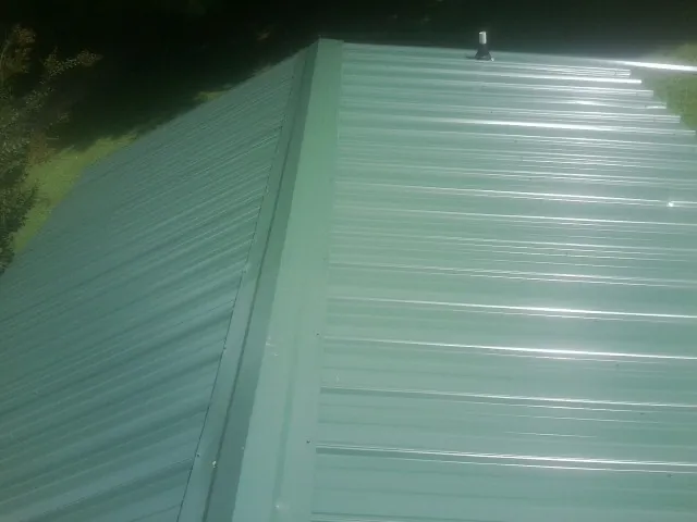 New green metal panels meeting at the ridge of a roof — Flat Roof Repair work by our crew in Reinholds