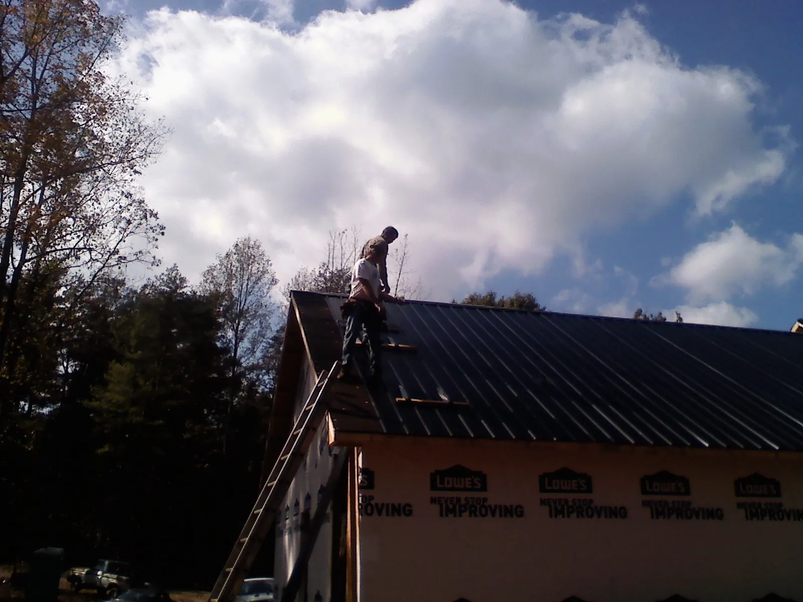Roofer fastening dark metal panels high against a cloudy sky, from a Roof Inspection job in Reinholds