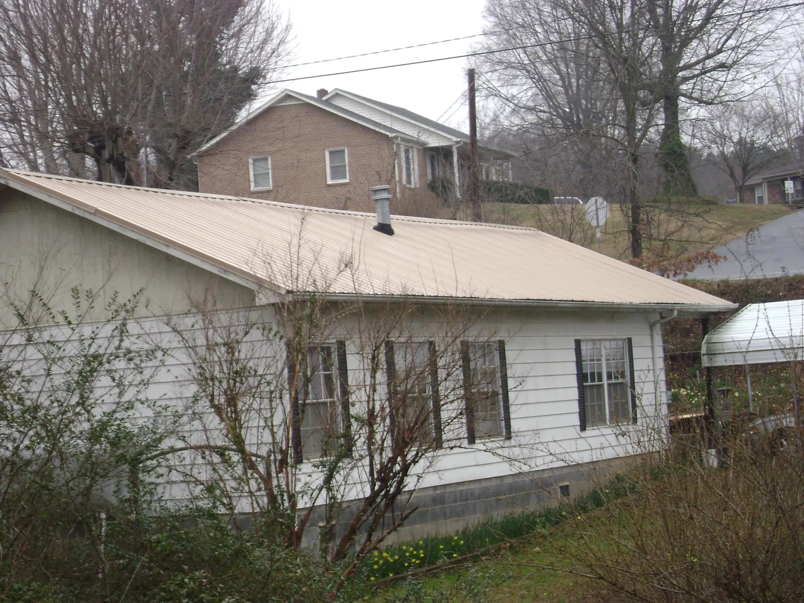 Tan metal roof on a white sided house set into a hillside — Commercial Roofing by Roofing Brothers in Reinholds